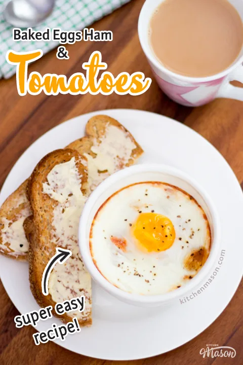 A small white bowl of baked eggs, ham and tomatoes on a white plate with toast and butter. Set on a deep wooden backdrop with a cup of tea, a green checked tea towel and a spoon.