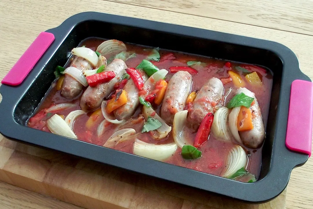 sausages, red pepper, orange pepper & onion in a baking tray with tinned tomatoes and basil