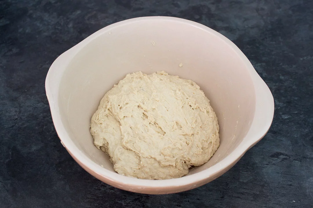 Slightly plump no knead bread dough in a large mixing bowl after a first prove