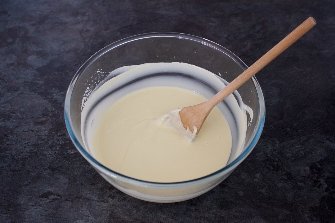 melted white chocolate in a large glass bowl with a wooden spoon