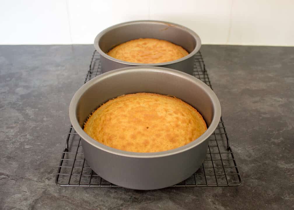 Baked Victoria Sandwich Cake sponges in two round cake tins on a cooling rack