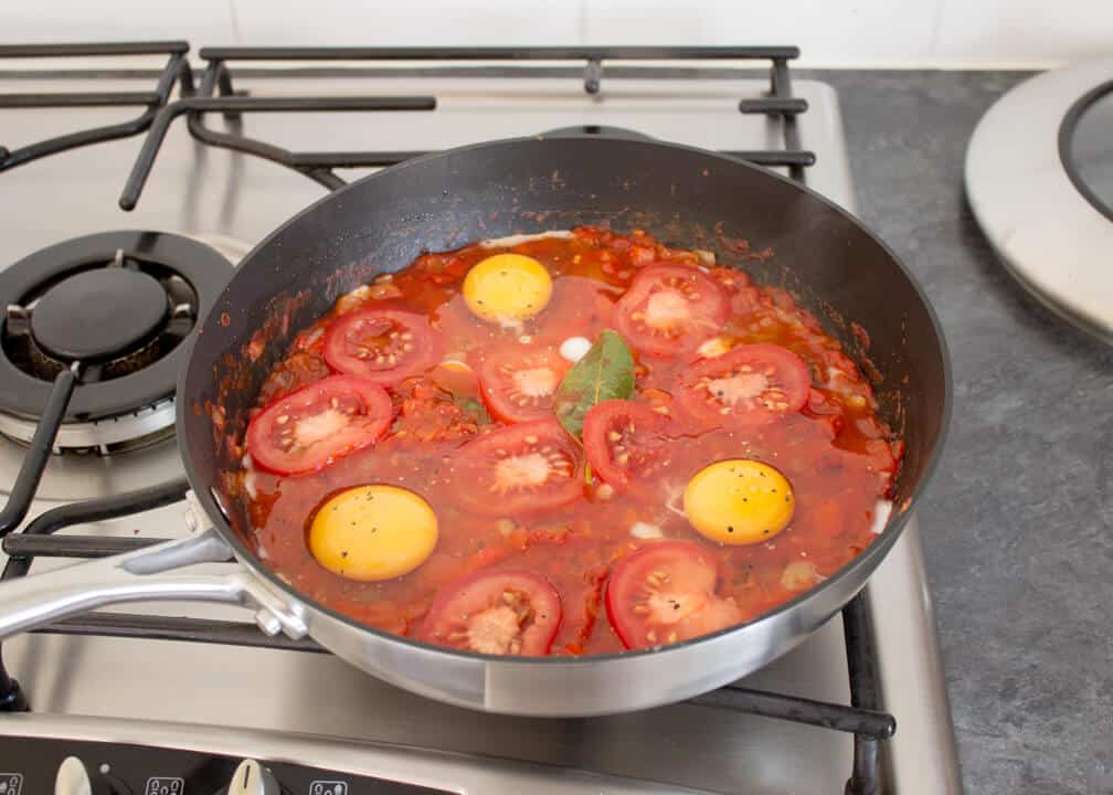 A tomato sauce in a pan being topped with eggs and tomatoes