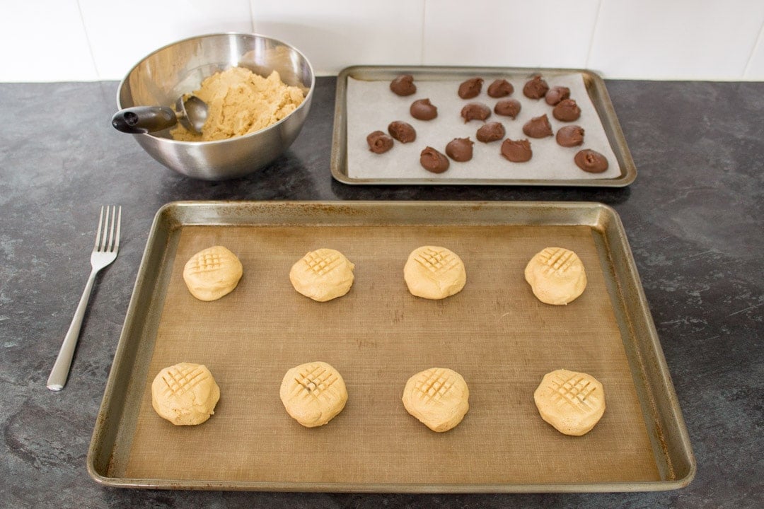 frozen nutella blobs wrapped in peanut butter cookie dough, spaced out on a lined baking tray