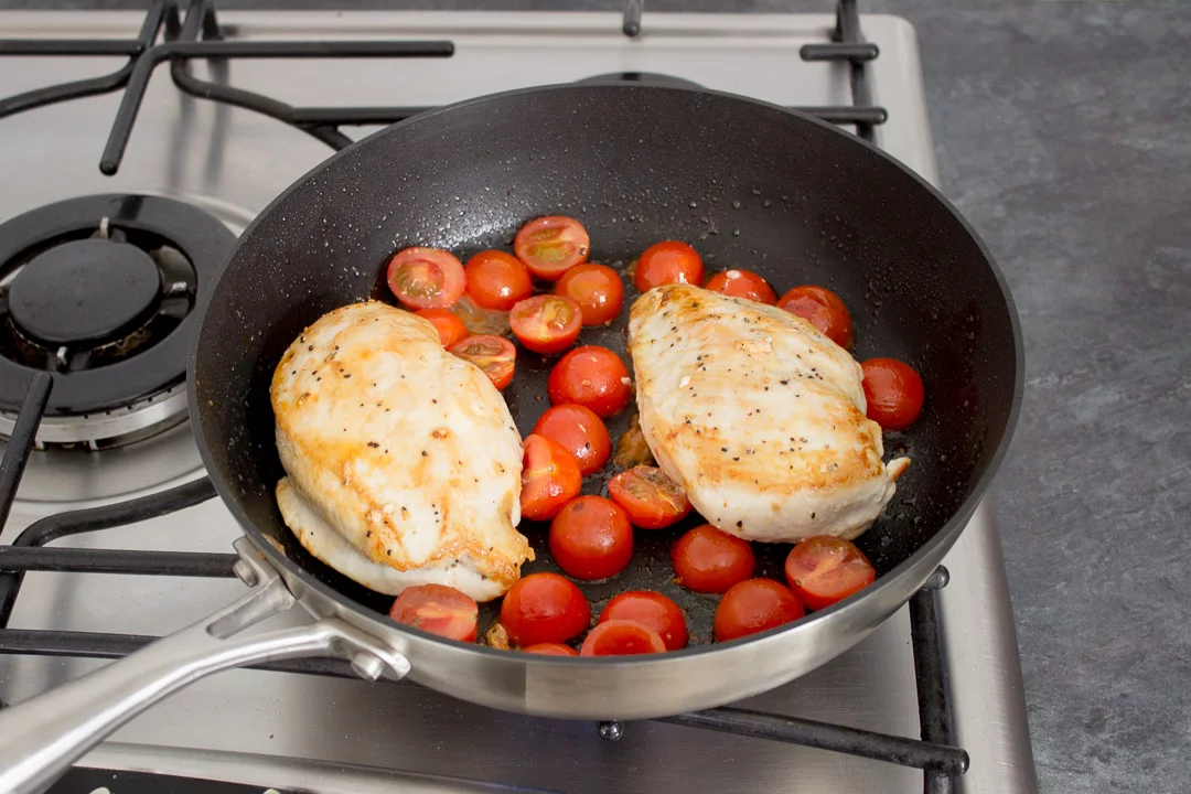 2 chicken breasts frying in a frying pan with cherry tomatoes