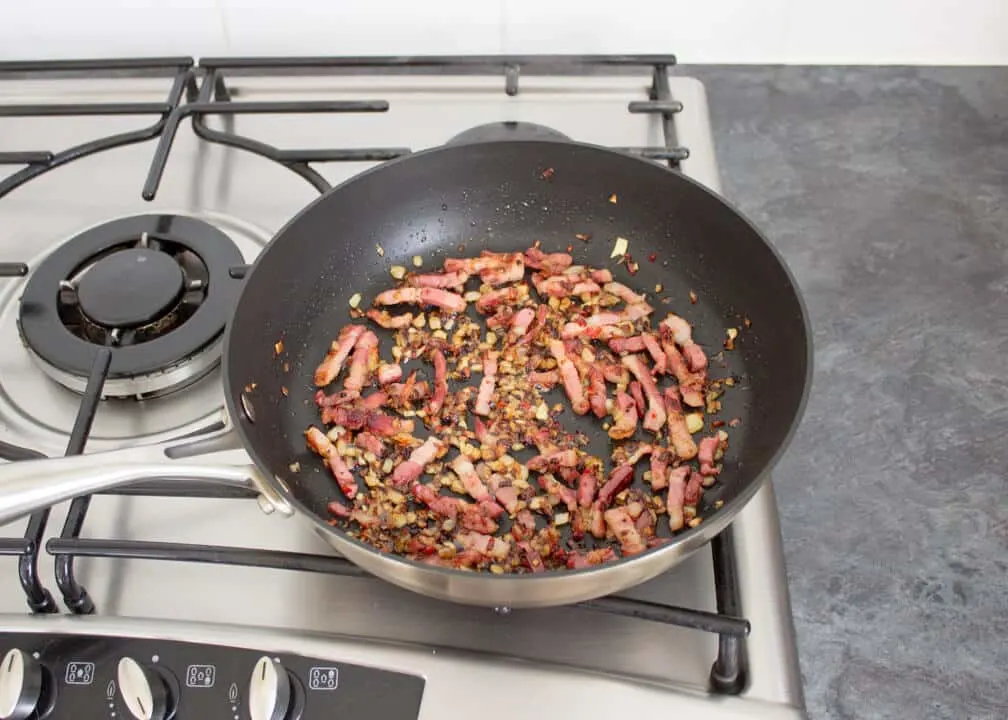Onion, chilli and pancetta frying in a pan