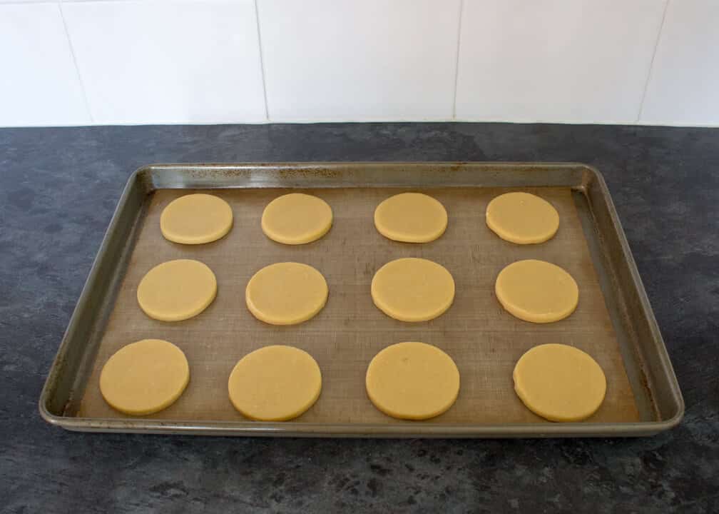 Unbaked cookies on a lined baking tray on a kitchen worktop.
