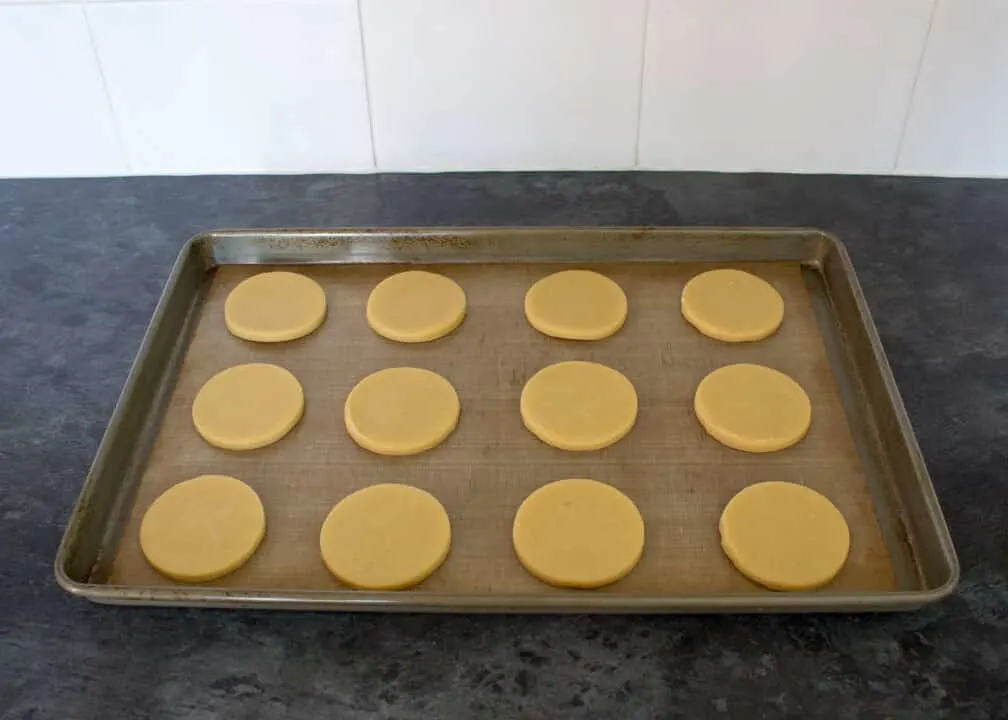 Unbaked cookies on a lined baking tray on a kitchen worktop.