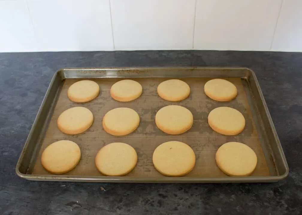 Baked cookies on a lined baking tray on a kitchen worktop.