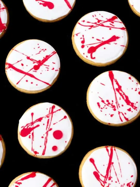 Flat lay view of lots of blood spatter halloween cookies lay on a black backdrop.