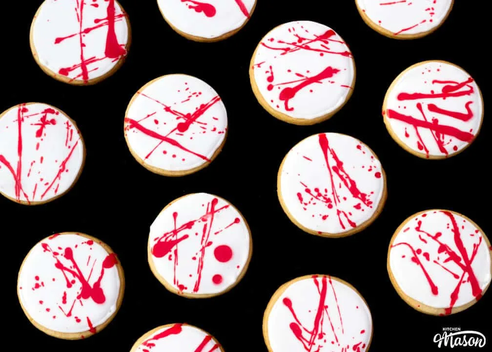 Flat lay view of lots of blood spatter halloween cookies lay on a black backdrop.