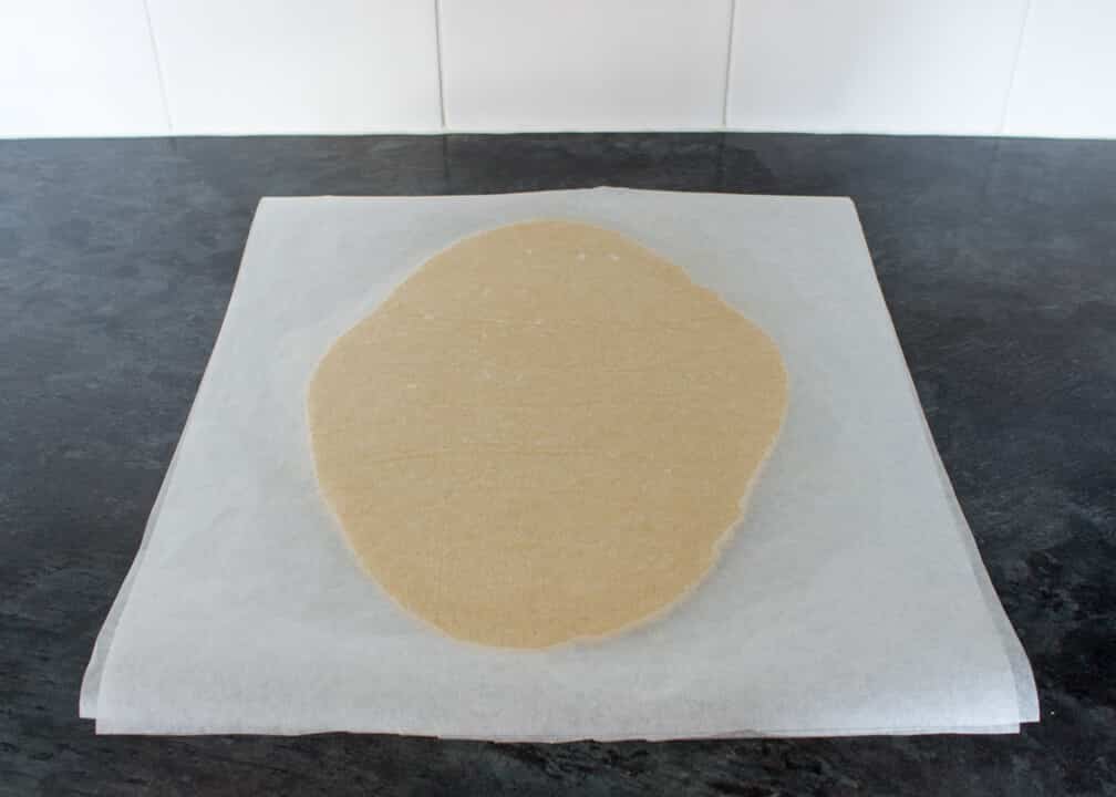 Cookie dough rolled out between two sheets of baking paper on a kitchen worktop.