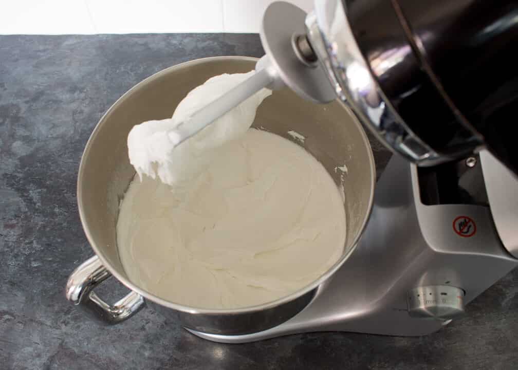 Egg whites, icing sugar and lemon juice whisked to stiff peaks in an electric stand mixer on a kitchen worktop.