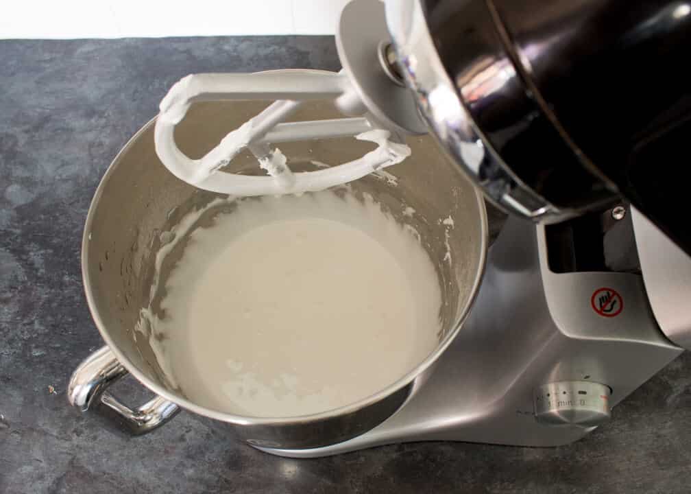 Egg whites, icing sugar and lemon juice that's been whisked to stiff peaks and thinned with water to a flooding consistency in an electric stand mixer on a kitchen worktop.