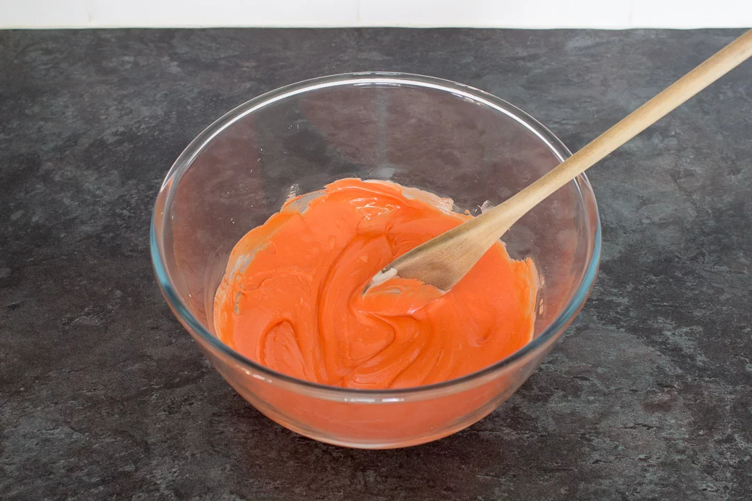 Melted white chocolate, dyed orange, in a bowl with a wooden spoon