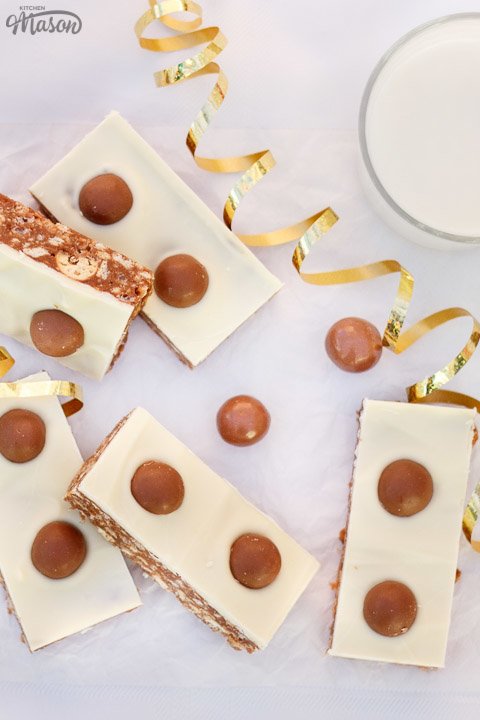 Malteser Tiffin Bars, a glass of milk and gold curling ribbon lay on a table.
