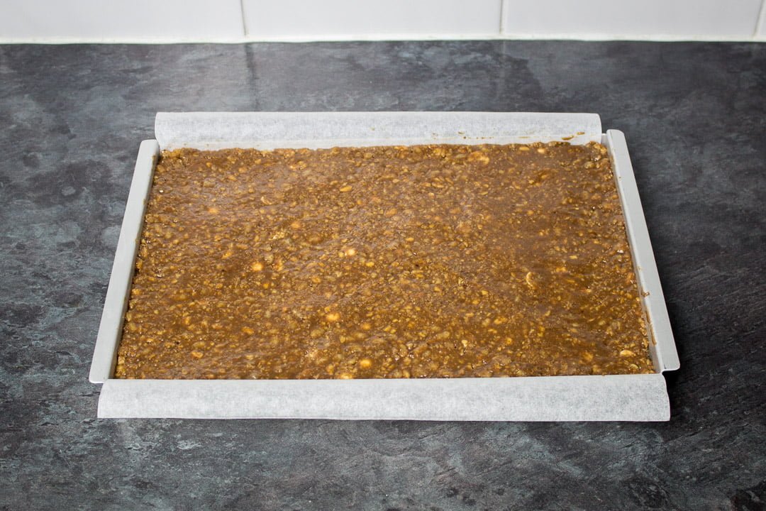 Malteser tiffin mixture pressed into a rectangular baking tin lined with baking paper