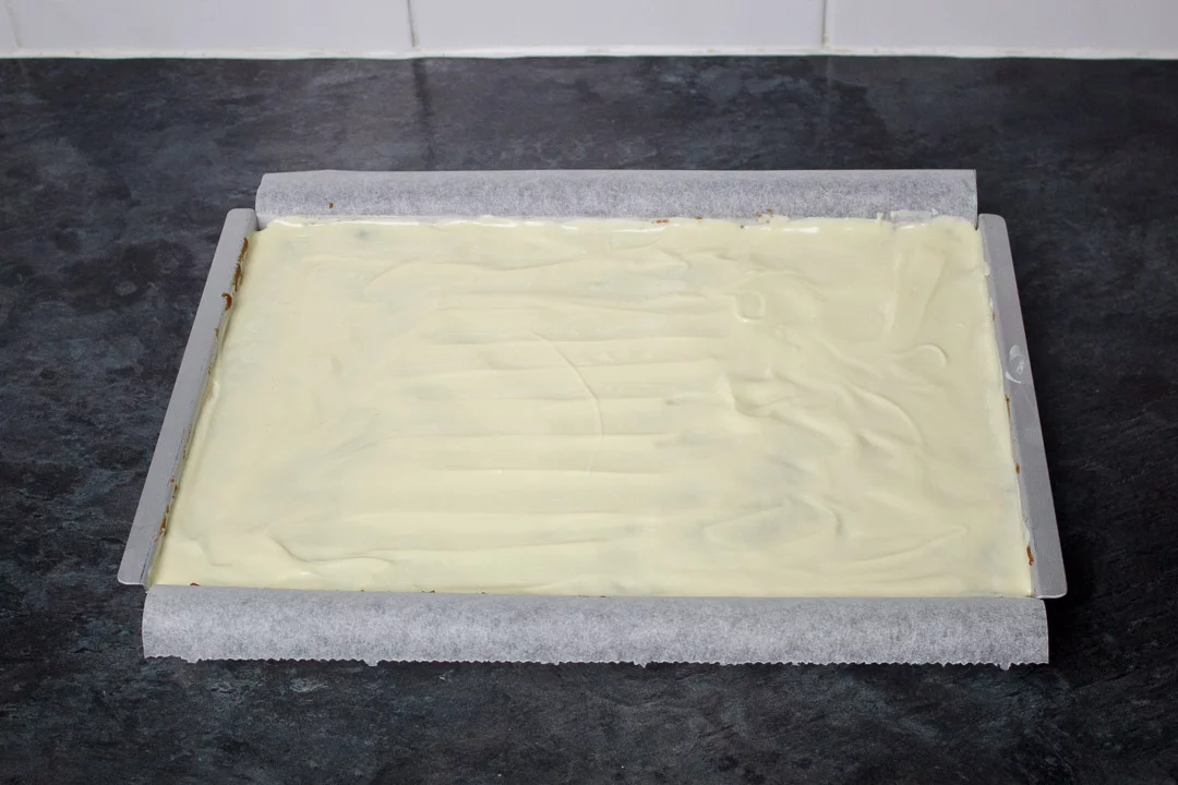 Melted white chocolate spread over the Malteser tiffin mixture in a rectangular baking tin