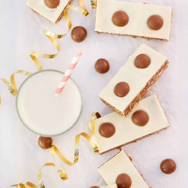 Malteser Tiffin Bars, a glass of milk and gold curling ribbon lay on a table.