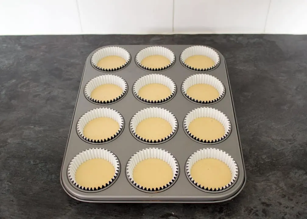 Cupcake batter divided between 12 cupcake cases in a tin