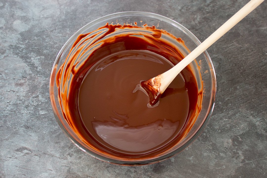 melted chocolate and butter in a glass bowl with a wooden spoon