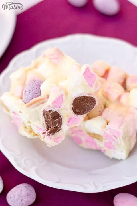 Mini Egg rocky road bars on a white plate with Mini Eggs scattered around.