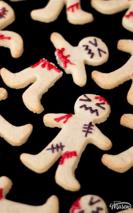 Flat lay view of lots of decorated ginger-dead men Halloween biscuits against a black background.