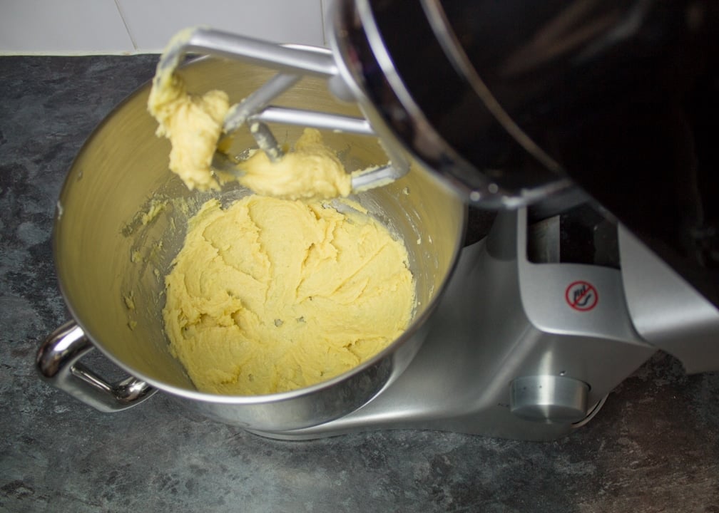 Creamed butter, sugar, egg yolk and water in an electric stand mixer on a kitchen worktop.
