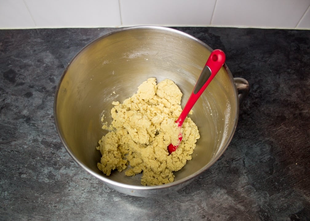 Ginger-dead men Halloween biscuit dough in a metal bowl on a kitchen worktop with a red spatula.