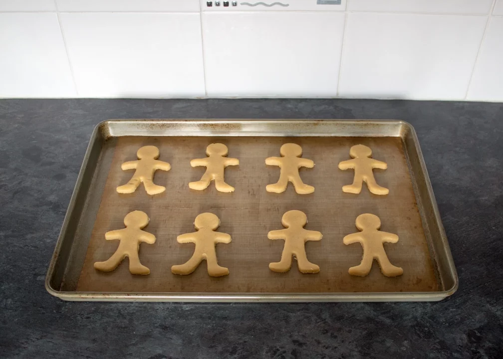 Gingerbread men on a lined baking tray on a kitchen worktop.