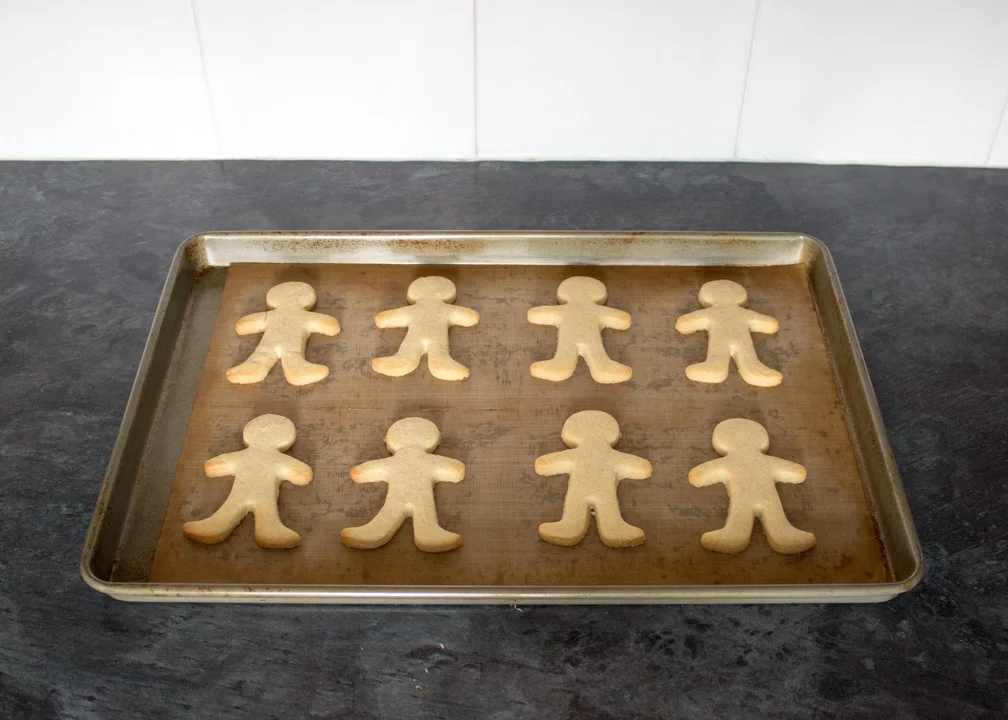 Baked gingerbread men on a lined baking tray on a kitchen worktop.