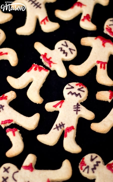 Flat lay view of lots of decorated ginger-dead men Halloween biscuits against a black background.