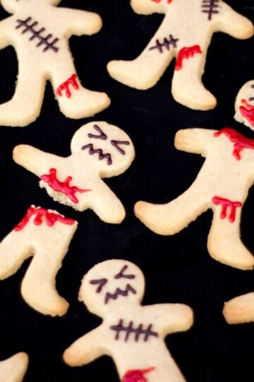 Flat lay view of lots of decorated ginger-dead men Halloween biscuits against a black background.
