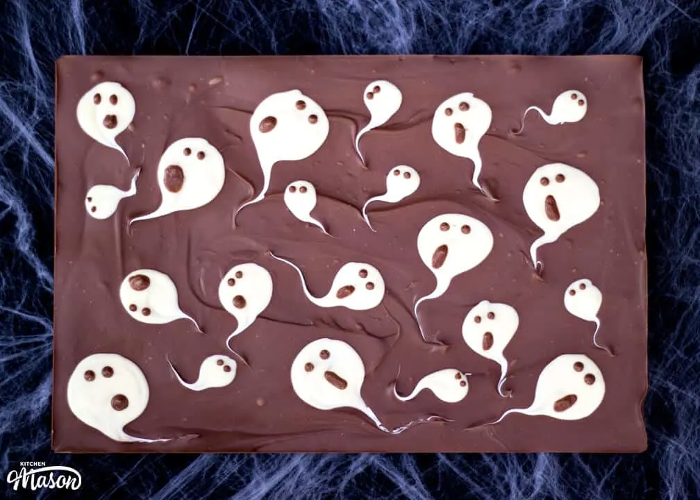 A whole slab of milk chocolate ghost halloween bark laid on a cobweb covered black piece of fabric.
