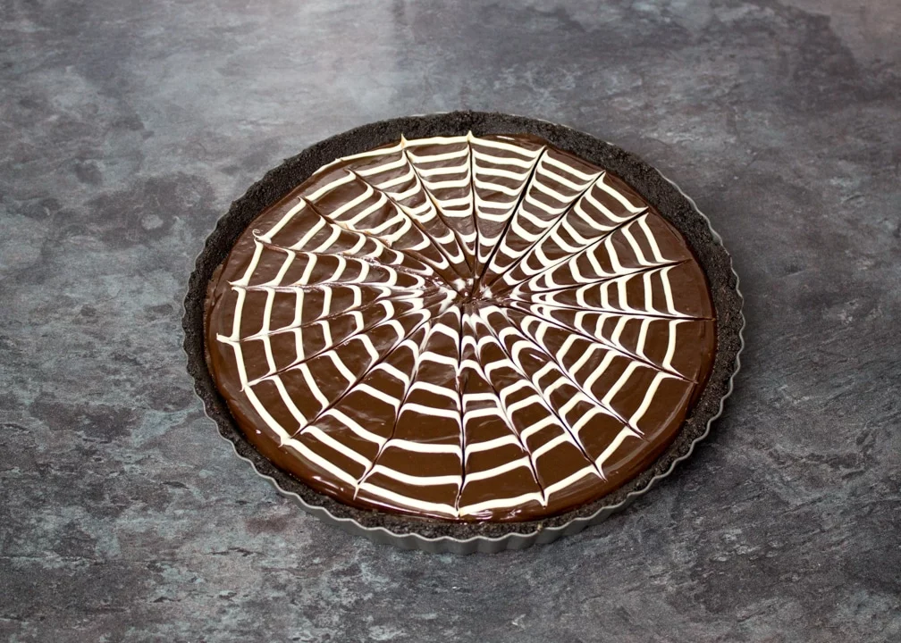 White chocolate spider web pattern skewered on top of a chocolate tart