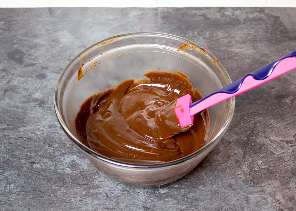 dark chocolate ganache in a glass bowl with a spatula