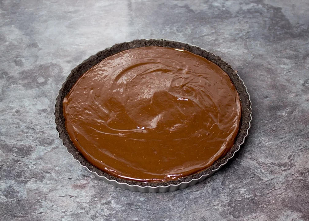 Dark chocolate ganache poured over the Oreo crust in a fluted tin