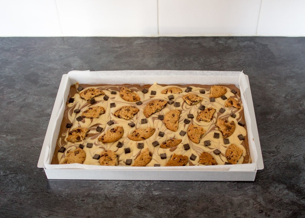 Peanut Butter Cookie Bark: melted milk chocolate in a baking tin with peanut butter chocolate swirled on top and broken chocolate chip chookies