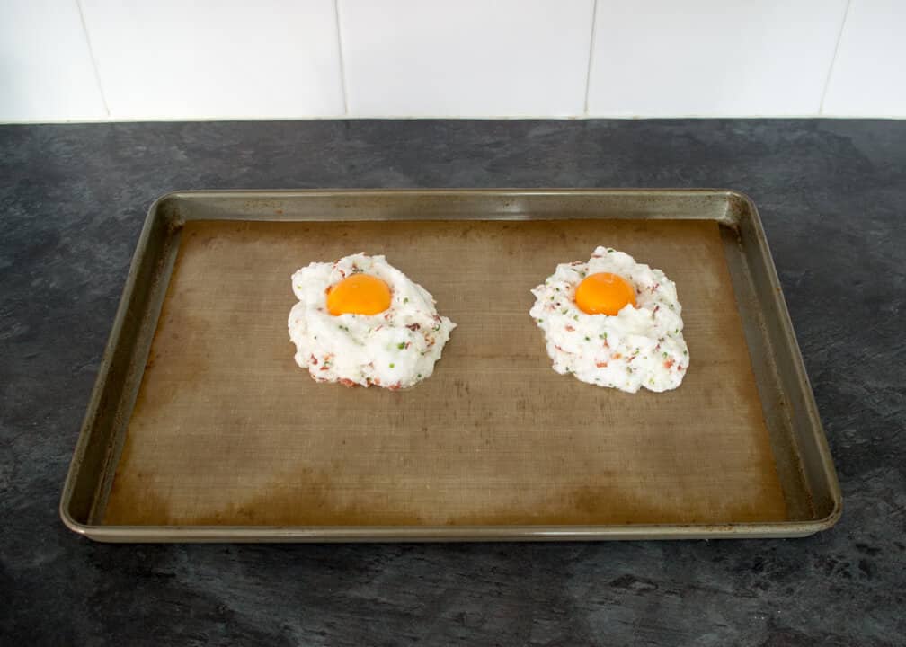 Bacon chive parmesan egg whites spooned into mounds on a baking tray with egg yolks placed on top
