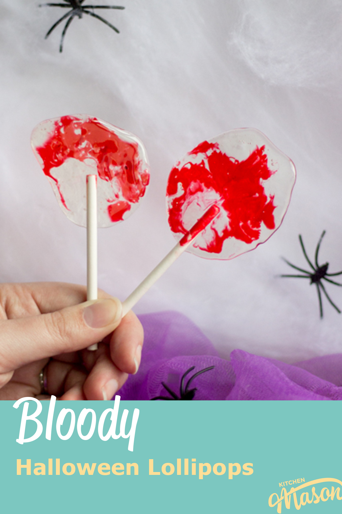 A hand holding 2 bloody Halloween lollipops against a white spider web background behind a base of purple netting. There are 3 black plastic spiders scattered around. A text overlay says "bloody Halloween lollipops".