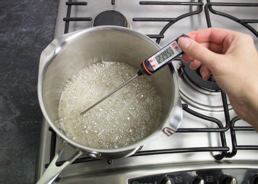 Sugar, cream of tartar and water in a saucepan boiling over a low heat on the stove top with a thermometer inside reading 239.5ºF