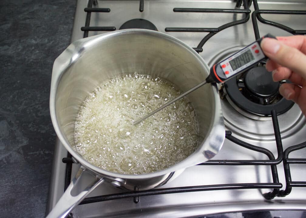 Sugar, cream of tartar and water in a saucepan boiling over a low heat on the stove top with a thermometer inside reading 304ºF