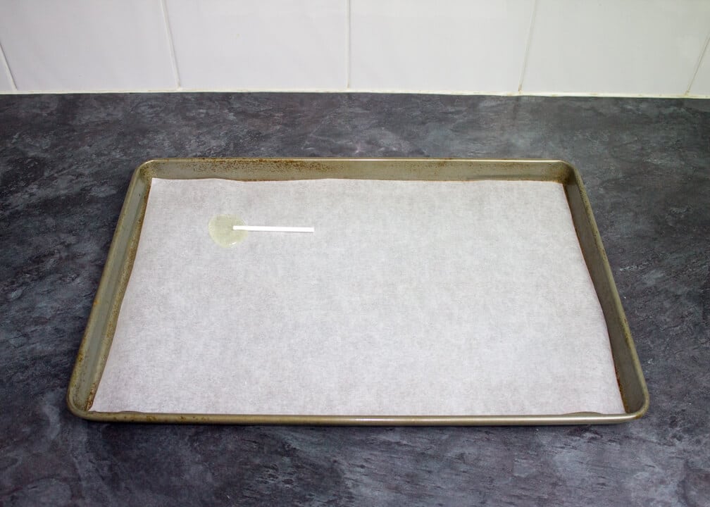A large baking tray lined with paper with a single lollipop on it.