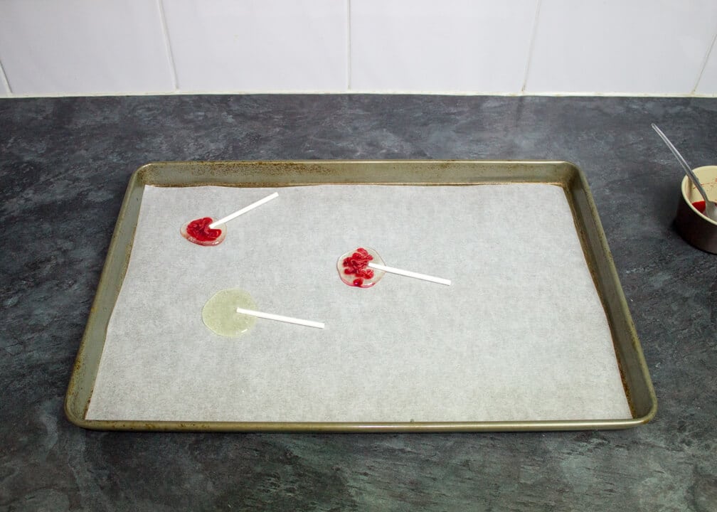 A large baking tray lined with paper with 2 bloody Halloween lollipops on it and 1 plain.