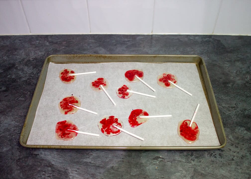 A large baking tray lined with paper with 10 bloody Halloween lollipops on it.