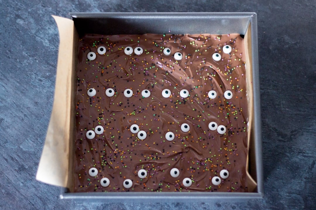 Edible eyes and halloween coloured sprinkles scattered over melted chocolate