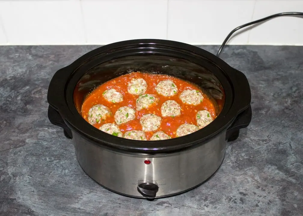 Uncooked meatballs in a sauce in a slow cooker