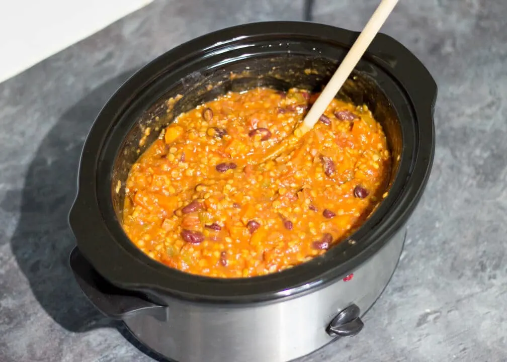 Cooked vegetarian chilli in a slow cooker with a wooden spoon