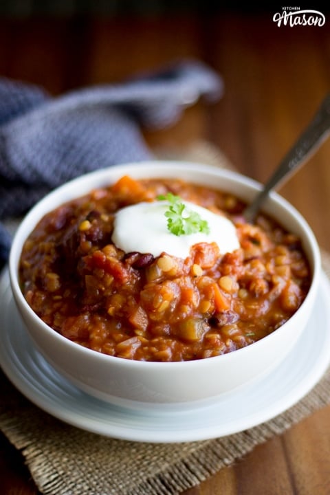 vegetarian chili in a bowl white topped with acidic cream and parsley