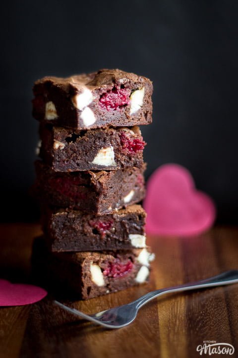 White chocolate raspberry brownies in a stack on a wooden worktop