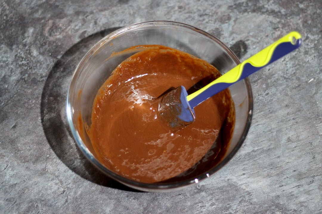 Melted chocolate, butter and eggs in a glass bowl with a rubber spatula